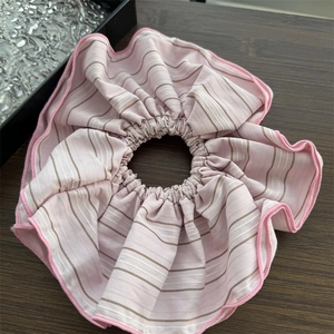 Detailed view of large pink striped scrunchie on dark wood surface with fabric texture