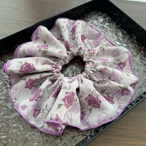 Dettaglio dell'elastico floreale con rose viola e bordi a onde su un vassoio nero