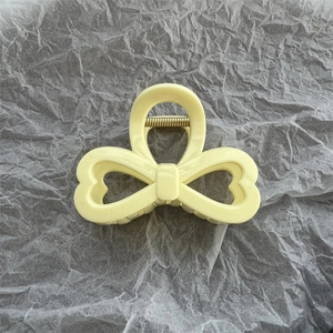 Dettaglio della pinza per capelli giallo crema a forma di fiocco con molla in metallo oro