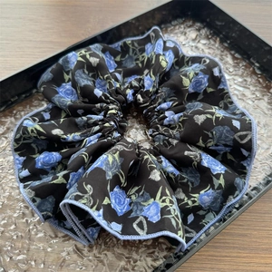 Dettaglio dell'elastico per capelli a fiori blu con bordo viola su vassoio a onde
