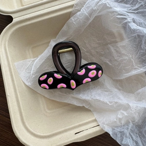 Detailed view of black claw clip with pink and green polka dots on white tissue paper