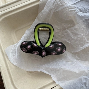 Detail of color-block hair claw clip featuring pink dots and a green handle design