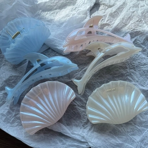 Detail of dolphin and shell hair claws in light blue and pink with pearlescent finish