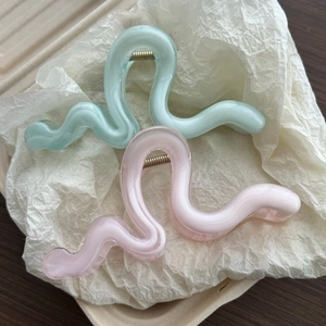 Close-up of translucent pastel pink and green hair claws with gold springs on wood