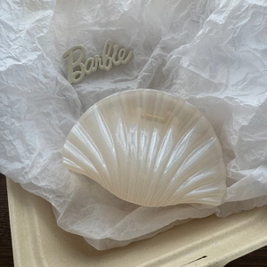 Detail of shell-shaped pearl white hair claw clip with iridescent finish on paper