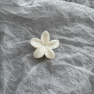 Detail of a pearlescent white flower hair claw clip with golden metal spring