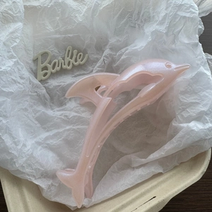 Detailed view of light pink dolphin hair claw clip with pearlescent finish on a tray