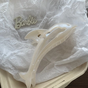 Detail of pearl white dolphin hair claw clip with golden metal spring on textured background