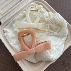 Detail view of two resin bow hair clips in milky white and pink colors with metal springs