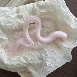 Close-up of a pink wave-shaped hair claw clip with glossy finish on white paper