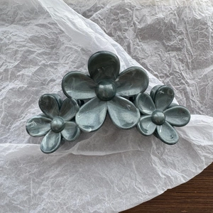 Close-up of three pearlescent flower hair claws with a shimmering silver grey finish
