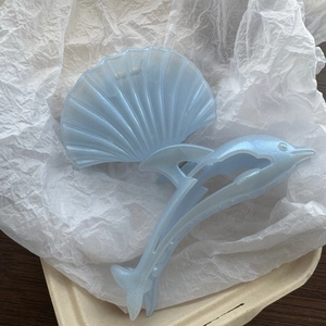 Detail showing the pearlescent light blue dolphin and shell hair claw clip with a glossy finish