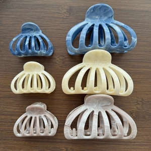 Flat lay of marble texture hair claw clips in blue, cream, and pink on dark wood surface