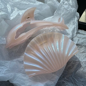 Close-up of glittery pink dolphin and shell hair claws on white tissue paper