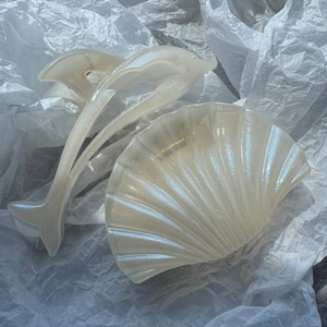 Detail view of pearlescent dolphin and seashell hair claw clips on white paper