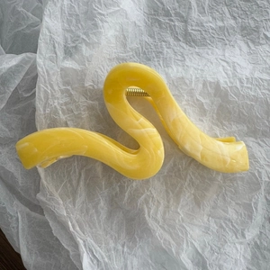 Dettaglio della pinza per capelli giallo marmo con molla dorata su carta materica