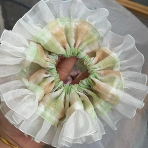 Detailed view of plaid fabric scrunchie with white ruffled tulle trim and green pattern