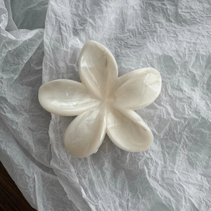 Dettaglio della molletta per capelli a forma di fiore di frangipane bianco crema marmorizzato