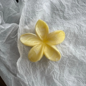 Dettaglio della pinza per capelli gialla a forma di plumeria con trama effetto marmo