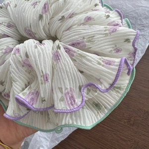 Close-up of beige pleated scrunchie with purple rose print and mint scalloped edges
