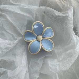 Close-up of a light blue flower hair claw clip with glossy resin petals on white paper