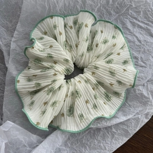 Close-up of a large white floral pleated scrunchie with green wavy edges and rose pattern