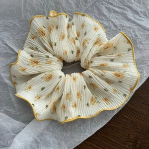 Detailed view of cream floral scrunchie with yellow trim and soft pleated fabric texture