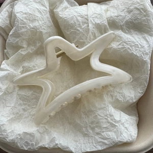 Dettaglio del fermaglio per capelli a stella bianco crema con molla in metallo oro