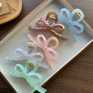Detail view of five colorful bow-shaped hair claws in iridescent acetate on a wooden tray