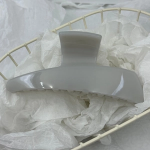 Minimalist grey trapezoidal hair claw clip resting on a white mesh basket and paper