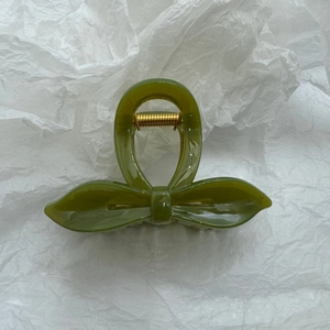 Détail d'une pince à cheveux en résine vert olive avec nœud et ressort en métal doré