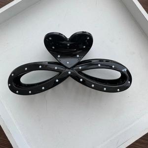 Detailed top view of black heart hair claw clip with white polka dots on white tray