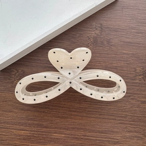 Macro detail of cream white heart hair claw clip with black polka dots on wooden desk