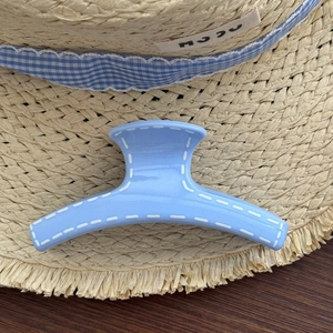 Close-up of light blue hair claw clip with white stitching on a summer straw hat