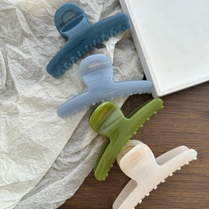 Set of four glossy pastel hair claws in navy, blue, olive, and cream on a wooden desk