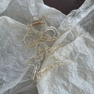 Detail view of clear star and bow hair claw clips with gold springs on white paper