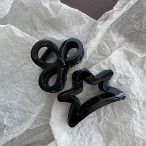 Close-up of gloss black star and bow-shaped hair claw clips on white paper background