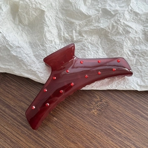 Detail of burgundy translucent claw clip with red rhinestones on a wooden background