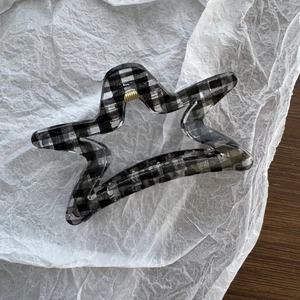 Detail of star-shaped hair claw clip with black and white checkered pattern and gold spring