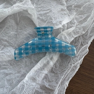 Macro detail of large hair claw clip featuring light blue plaid pattern on acrylic material
