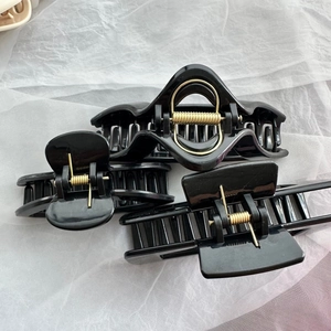Detailed view of three black hair claw clips with strong gold metal springs on white fabric