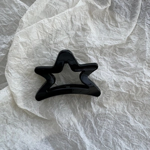 Detail of a high-gloss black hollow star hair claw clip on a white textured backdrop