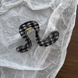 Detail of checkered S-shaped hair claw clip showing golden spring and acetate texture
