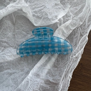 Detailed top view of light blue checkered acetate hair claw clip on soft paper