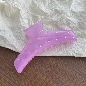 Detail of a purple matte claw clip with sparkling rhinestones on textured wood background