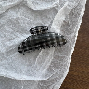 Detail of a large black and white gingham hair claw clip on white crinkled paper background