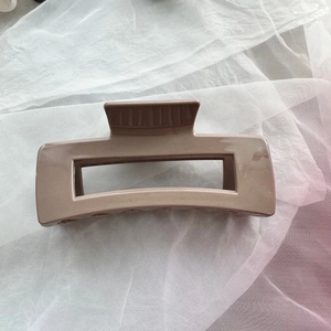 Detail of a dark khaki rectangular hair claw clip on soft white draped fabric