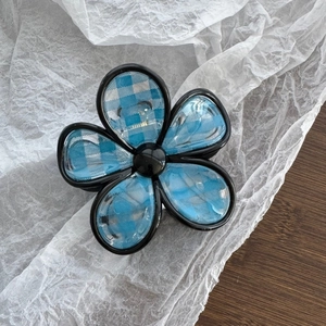 Detail view of flower-shaped hair claw with blue plaid pattern and black borders