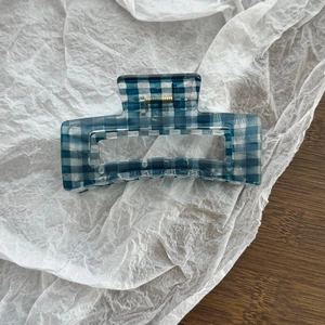 Detail of blue and white checkered hair claw clip with golden metal spring on a wooden desk