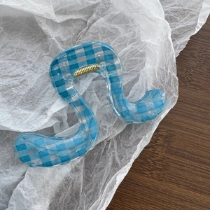 Macro detail of wave-shaped light blue checkered hair claw with gold spring